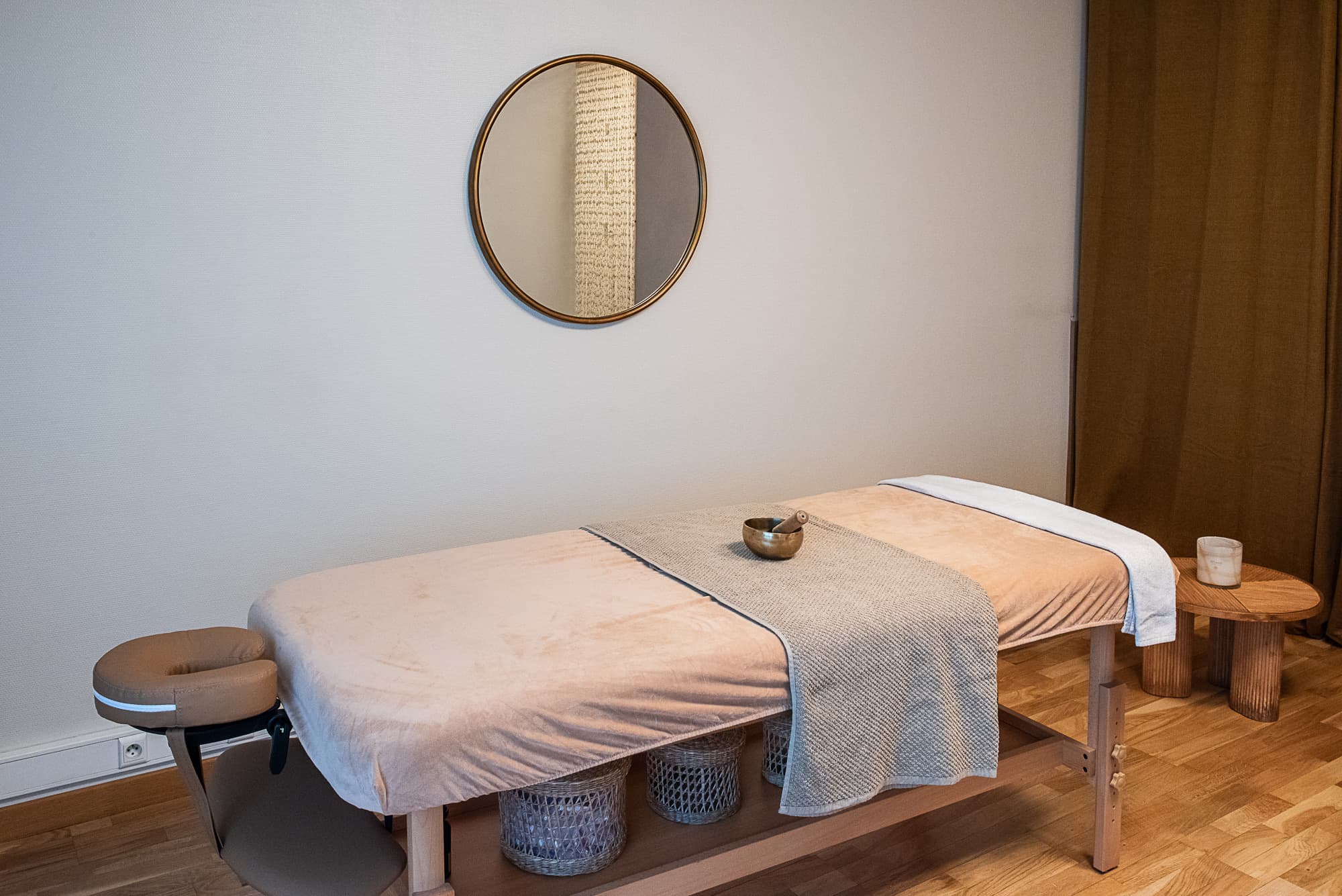 Table de massage sous un miroir doré, bol chantant posé sur le linge